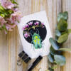 Carte illustrée d'un scarabée vert émeraude entouré de fleurs de magnolia roses, fond noir, style coloré et précis