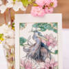 Carte illustrée Héron bleu et magnolias 3 Carte illustrée d'un héron aux plumes bleutées et grises entouré de magnolias roses et de motifs asiatiques, style aquarelle, fond blanc